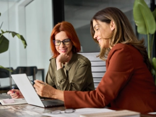 Two smiling young women reviewing work on a laptop